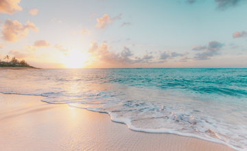 Sun setting against clear blue waters and a sandy beach